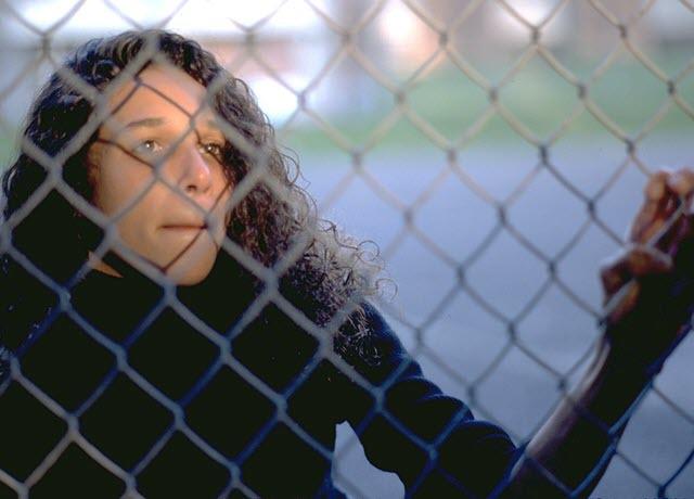 A young woman looking out the fence of a prison